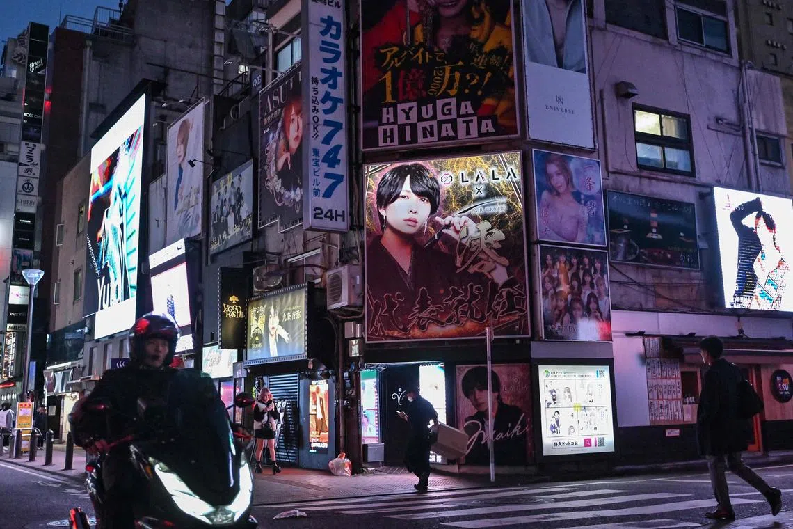 People walking past advertisements for bars and entertainment establishments, including some "host clubs", places which offer entertainment with male companions, along a street in the Kabukicho area of Shinjuku Ward in Tokyo. 