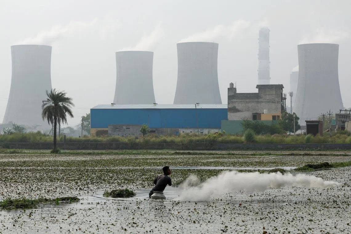 FILE PHOTO: A farmer sprinkles pesticide on the field as smoke rises from the chimneys of a coal power plant as the demand for coal-based power plants has risen due to the prolonged heatwave spells, in Dadri, India, June 20, 2024. REUTERS/ Priyanshu Singh/File Photo