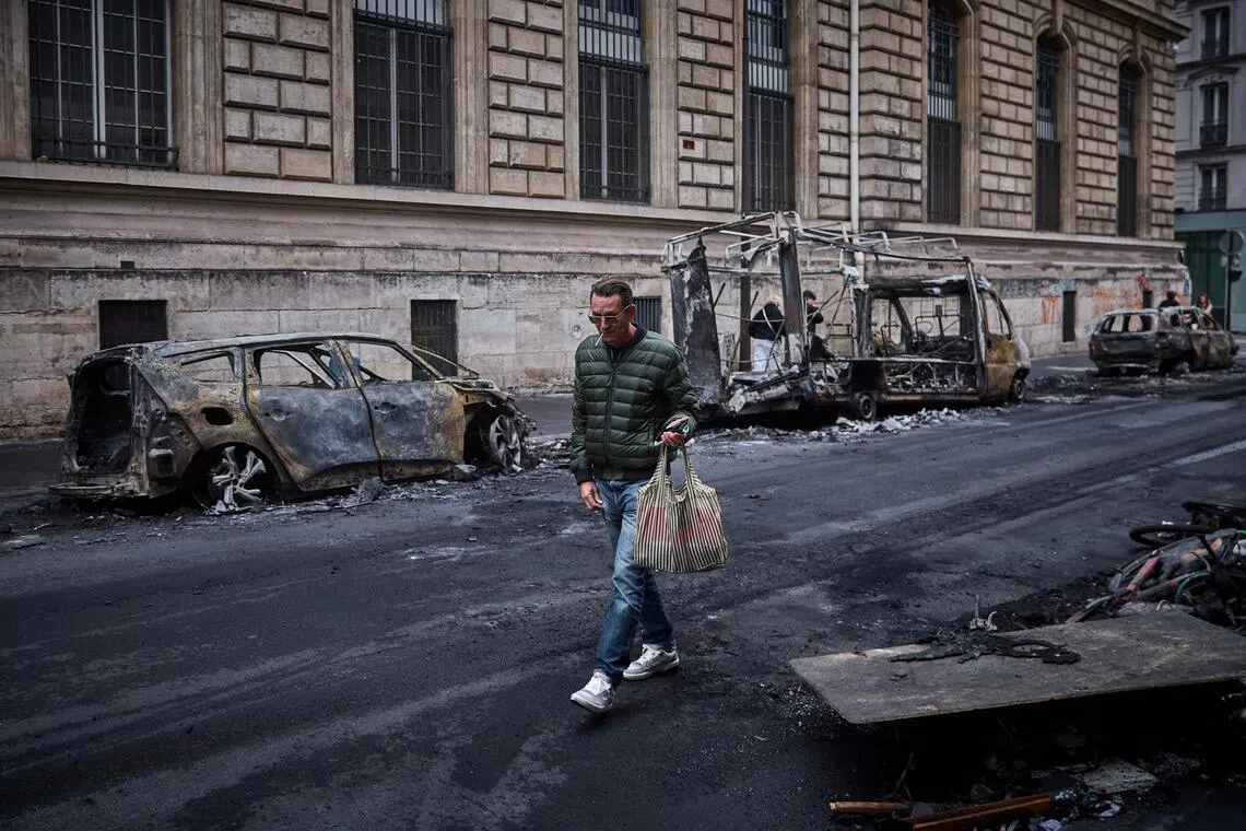 A man walks past a row of burnt out vehicles in Paris, two days after a nationwide protest and riots rocked France.