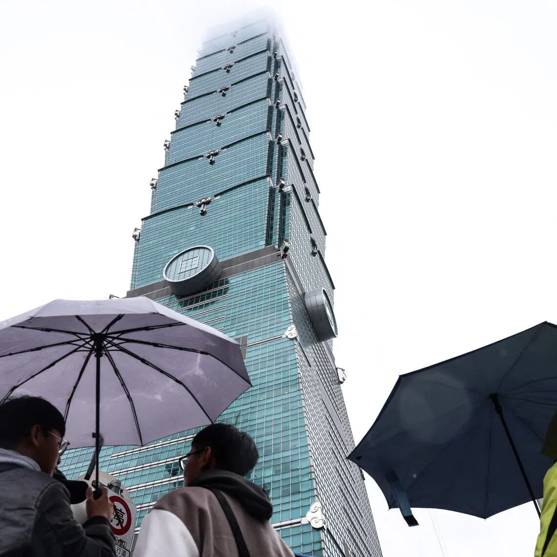 People holding umbrellas under the landmark Taipei 101 building, which US climber Alex Honnold was scheduled to scale but postponed due to bad weather, in Taipei on Jan 24, 2026. 