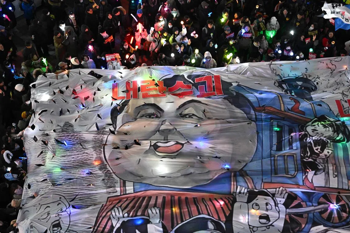 Protesters attending a candlelight vigil demanding the impeachment of South Korea President Yoon Suk Yeol hold up a banner showing a caricature of Yoon Suk Yeol outside the People Power Party headquarters in Seoul on December 13, 2024. South Korea's opposition leader on December 13, urged ruling party lawmakers to side with the "people" and impeach President Yoon Suk Yeol over his failed martial law bid, a day before a second parliamentary vote that appears on a knife edge. (Photo by Jung Yeon-je / AFP)