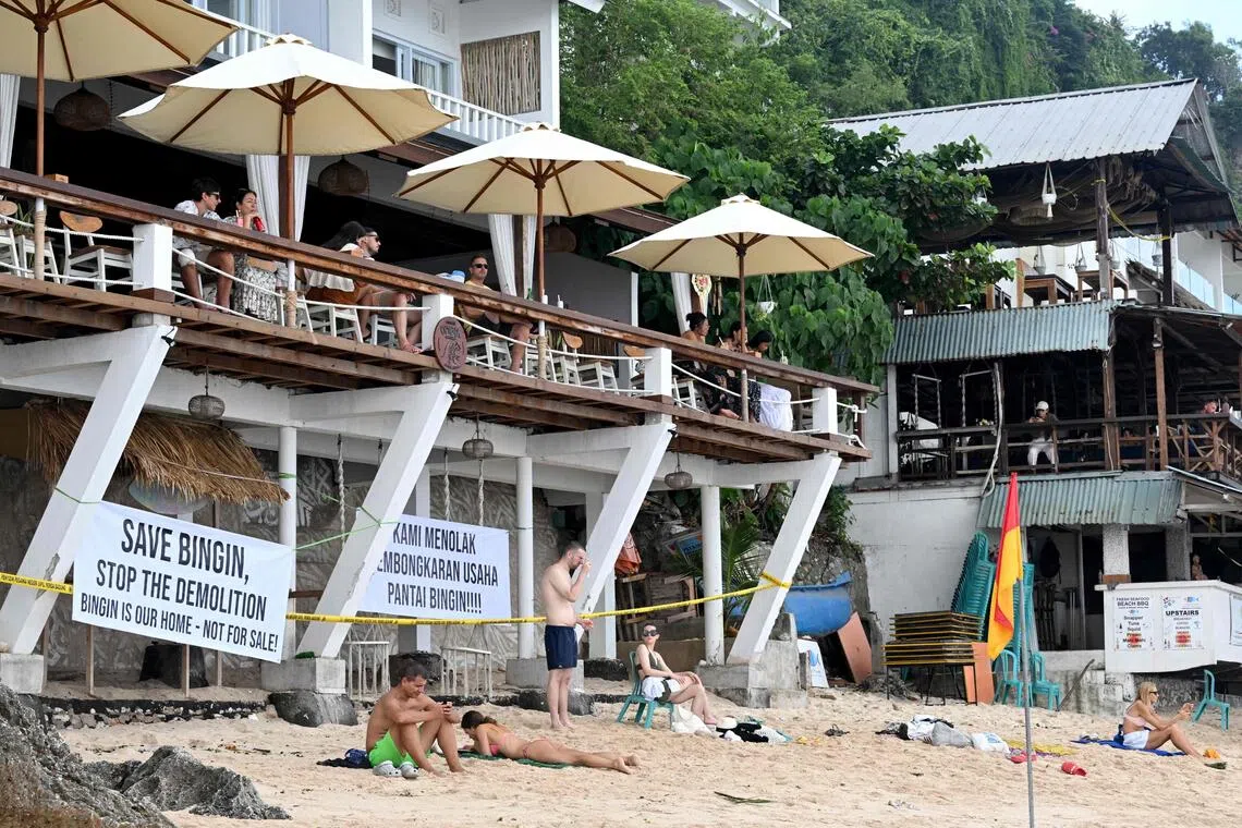 Tourist are seen in front of restaurants with police barricade tapes at Bingin Beach in the village of Pecatu in Badung Regency on Indonesia's resort island of Bali on July 23, 2025. Dozens of villas and restaurants that were built without acquiring the government's permission on the beach were demolished by the Badung district government in Bali province. (Photo by SONNY TUMBELAKA / AFP)
