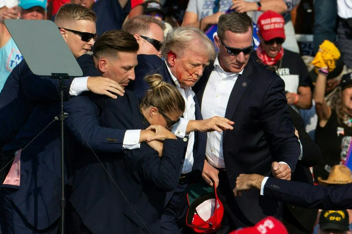 Former US President Donald Trump is seen with blood on his face surrounded by secret service agents as he is taken off the stage at a campaign event in Butler, Pennsylvania, on July 13, 2024.