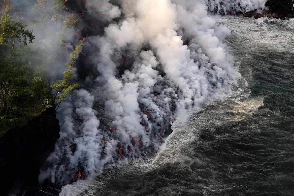 TOPSHOT - An aerial picture shows smoke rising as lava from the Piton de la Fournaise volcano reaches the ocean in Sainte-Rose, on the French Indian ocean island of Reunion, on March 16, 2026. The lava flow, which had stalled 150 metres from the ocean for several hours, finally reached the water on March 16, 2026 more than a month after the volcano began erupting on February 13, 2026. (Photo by Richard BOUHET / AFP)