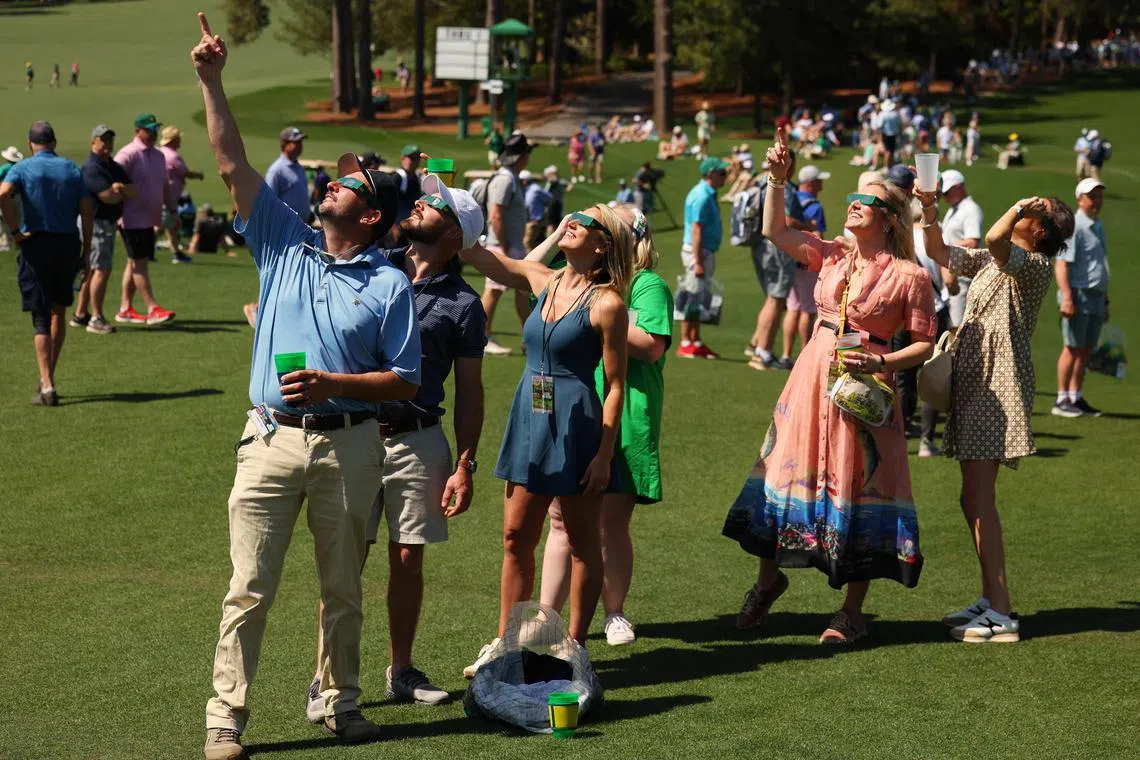 Patrons use glasses to view the eclipse during a practice round prior to the 2024 Masters.