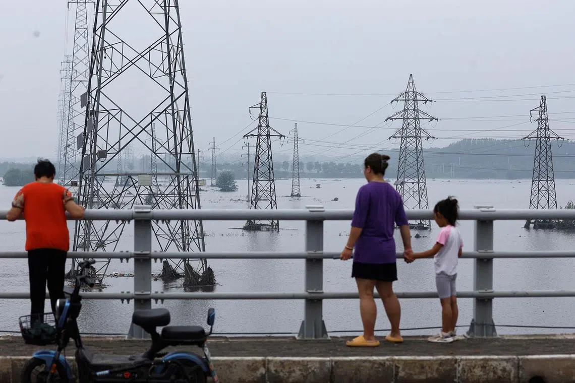 People look at electricity pylons in a flooded river after Typhoon Doksuri brought rains and floods in Beijing, China, August 2, 2023. 