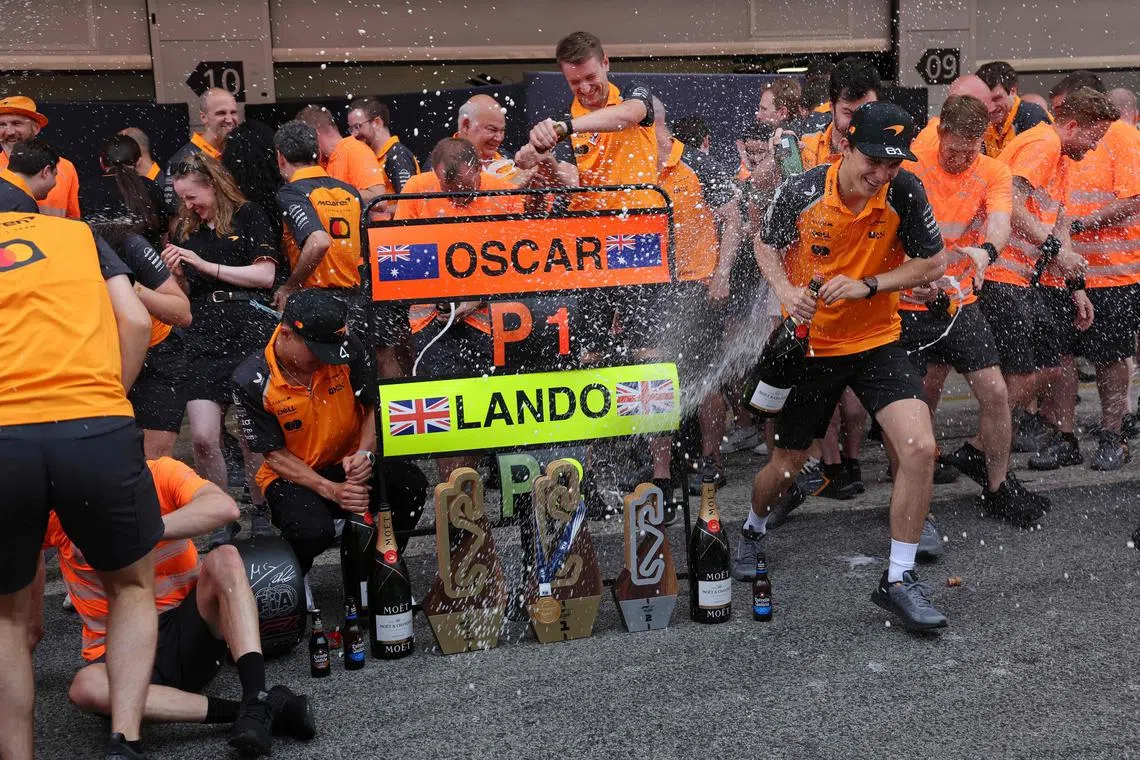 McLaren's Australian driver Oscar Piastri (right) and Lando Norris (left) are sprayed with champagne while posing for a team photo after the  Spanish Grand Prix.
