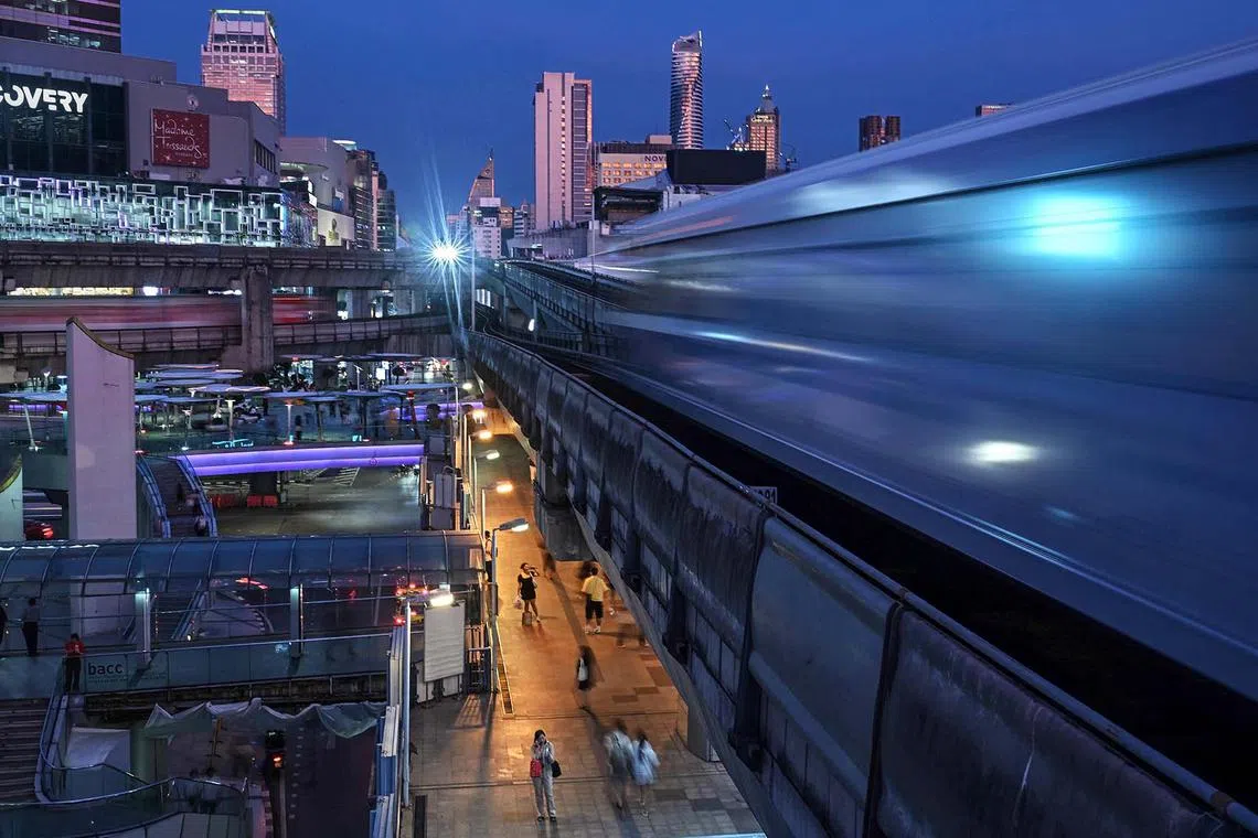 TOPSHOT - Pedestrians use the skywalk bridge between shopping malls as BTS trains pass above them in Bangkok on October 16, 2024. (Photo by Lillian SUWANRUMPHA / AFP)