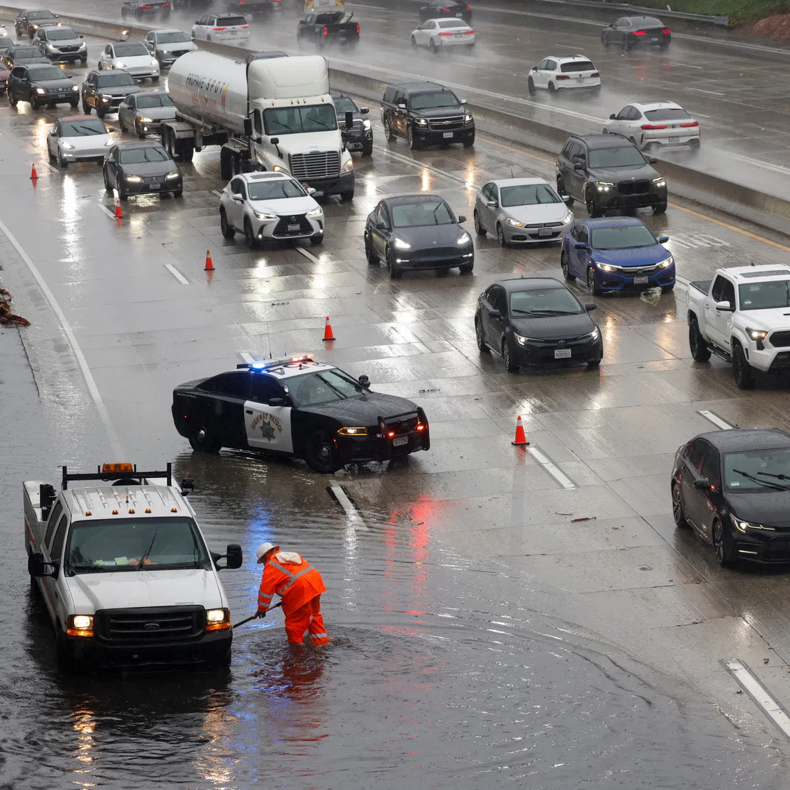 A worker clears debris from a flooded part of the 134 freeway, as heavy rains fall due to an atmospheric river in Burbank. 