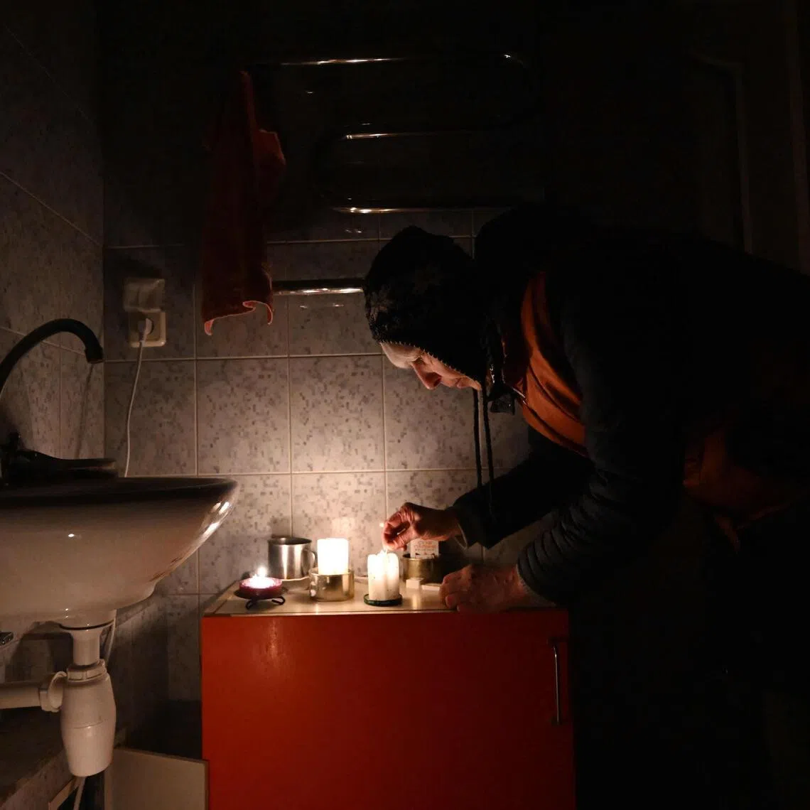 Ukrainian artist Oksana Gordiets, 67, lights candles to heat the bathroom and prevent the water in the pipes from freezing, in Kyiv, on Jan 25.