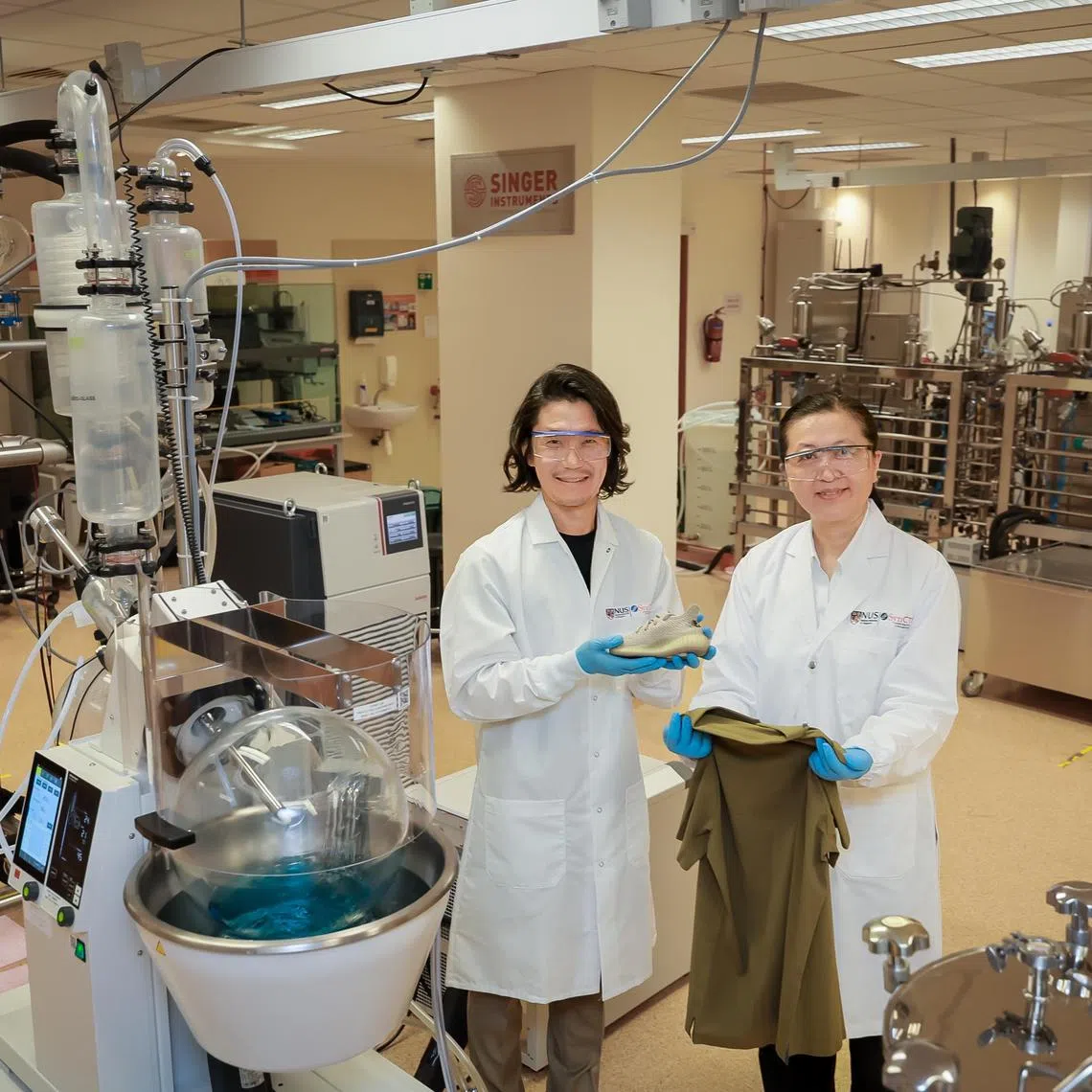 Professor Liu Bin (right), NUS Deputy President (Research and Technology) and Associate Professor Matthew Chang (left), Director, NUS SynCTI, with the finished products, a shoe and a shirt, in the pilot-scale lab at the NUS Centre For Life Sciences on Oct 10, 2024.