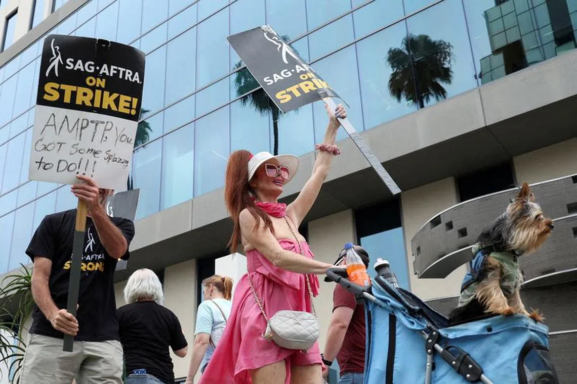 Phoebe Price holds a sign, while pushing a dog in a stroller, as SAG-AFTRA actors and Writers Guild of America (WGA) writers walk the picket line during their ongoing strike outside Sunset Bronson studios, near Netflix offices in Los Angeles, California, U.S., August 11, 2023. REUTERS/Mario Anzuoni/File photo