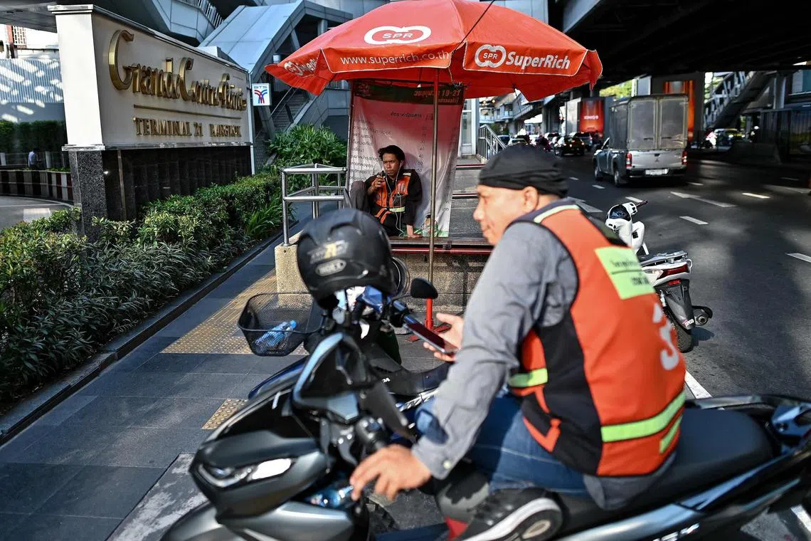 A motorbike taxi driver takes shelter from the sun under an umbrellas as he waits for customers in Bangkok on April 29, 2024. (Photo by MANAN VATSYAYANA / AFP)