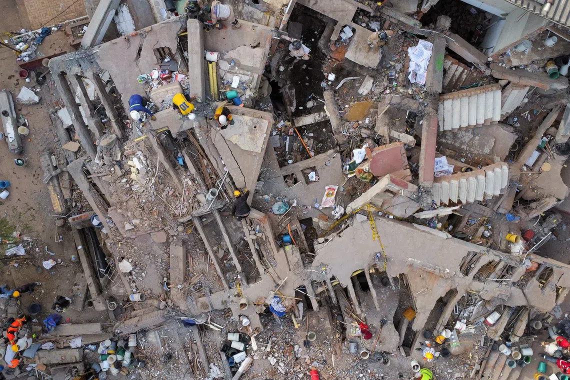 Aerial view of a severely damaged multi-story building with people amidst the rubble.