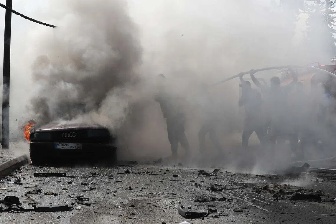 TOPSHOT - Lebanese firefighters put out a fire in a car after an Israeli strike in the southern city of Sidon on August 21, 2024. An Israeli strike in Lebanon's southern city of Sidon on August 21, killed a Fatah official, said a leader from the Palestinian group and a security source, marking the first such attack reported on Fatah in over 10 months of cross-border clashes. (Photo by Mahmoud ZAYYAT / AFP)