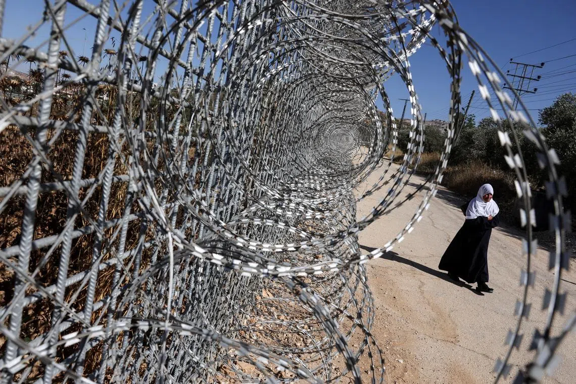 Jawaher Foqahaa walks past the tall metal fencing installed by the Israeli military that closed off four of the five entrances to their town and runs directly past the family home, in Sinjil, near Ramallah, in the Israeli-occupied West Bank, June 26, 2026. REUTERS/Ammar Awad