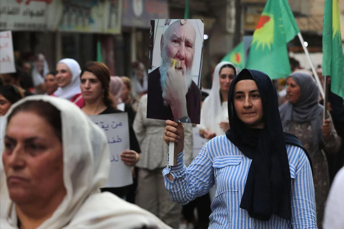 A Kurdish Syrian woman carrying an image of Sheikh Merhej Shahin, a Druze elder,  on July 17, after a video appeared online of a man in military attire forcibly shaving off the 80-year-old man's moustache. 
