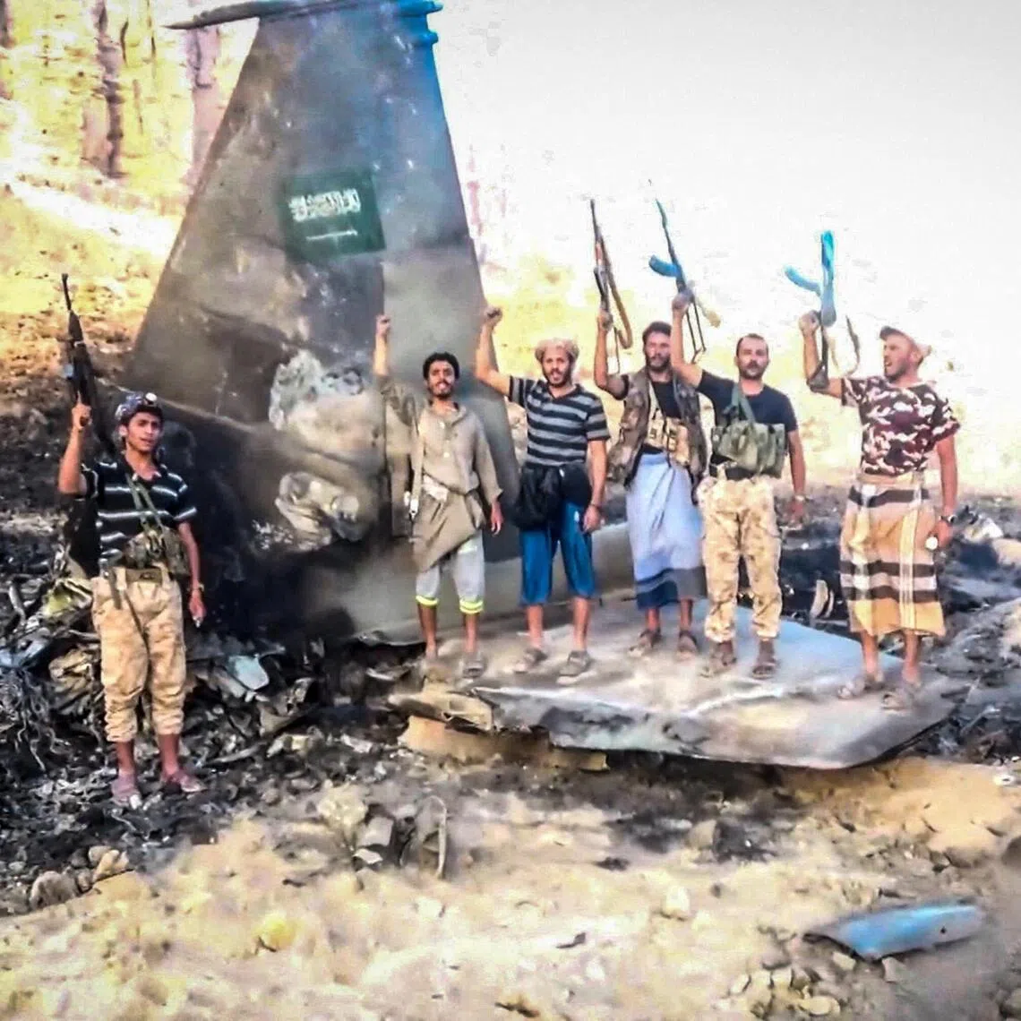 Houthi fighters standing in front of what they say is a downed Saudi jet, at a location given as Yemen.