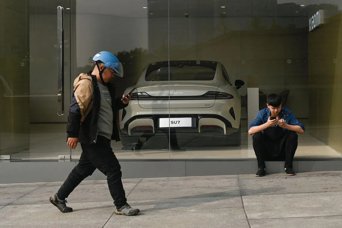 A man walks past a Xiaomi SU7 self-driving electric car displayed at a store in Beijing.