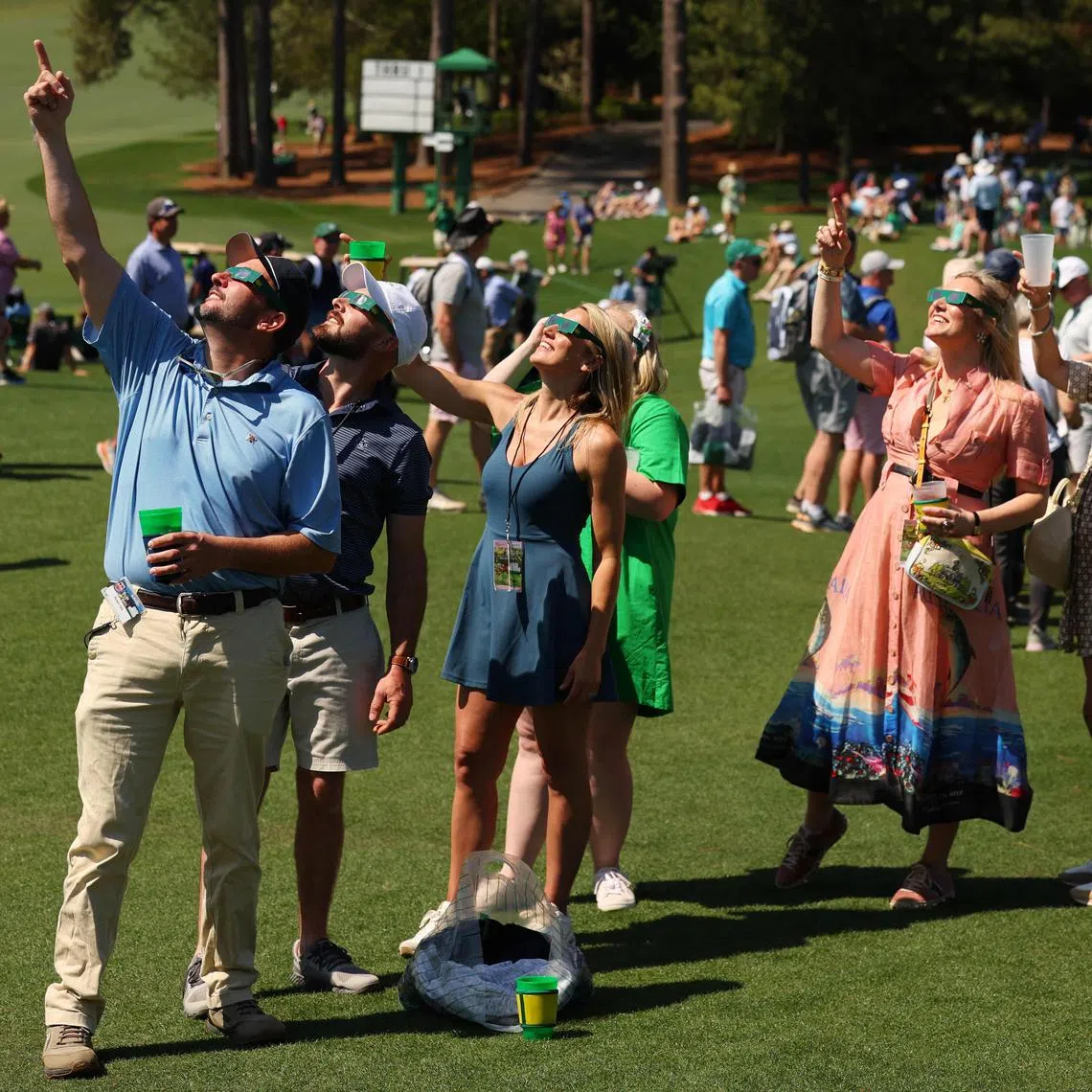 Patrons use glasses to view the eclipse during a practice round prior to the 2024 Masters.