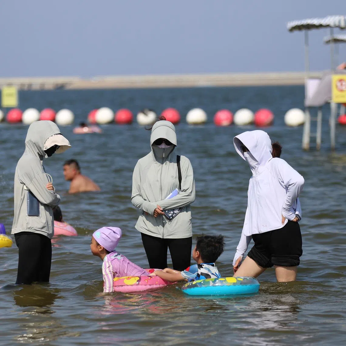 FILE PHOTO: Beachgoers wearing sun protection clothing play in the waters at a beach amid an orange alert for heatwave, on the outskirts of Shanghai, China August 9, 2024. REUTERS/Nicoco Chan/File Photo