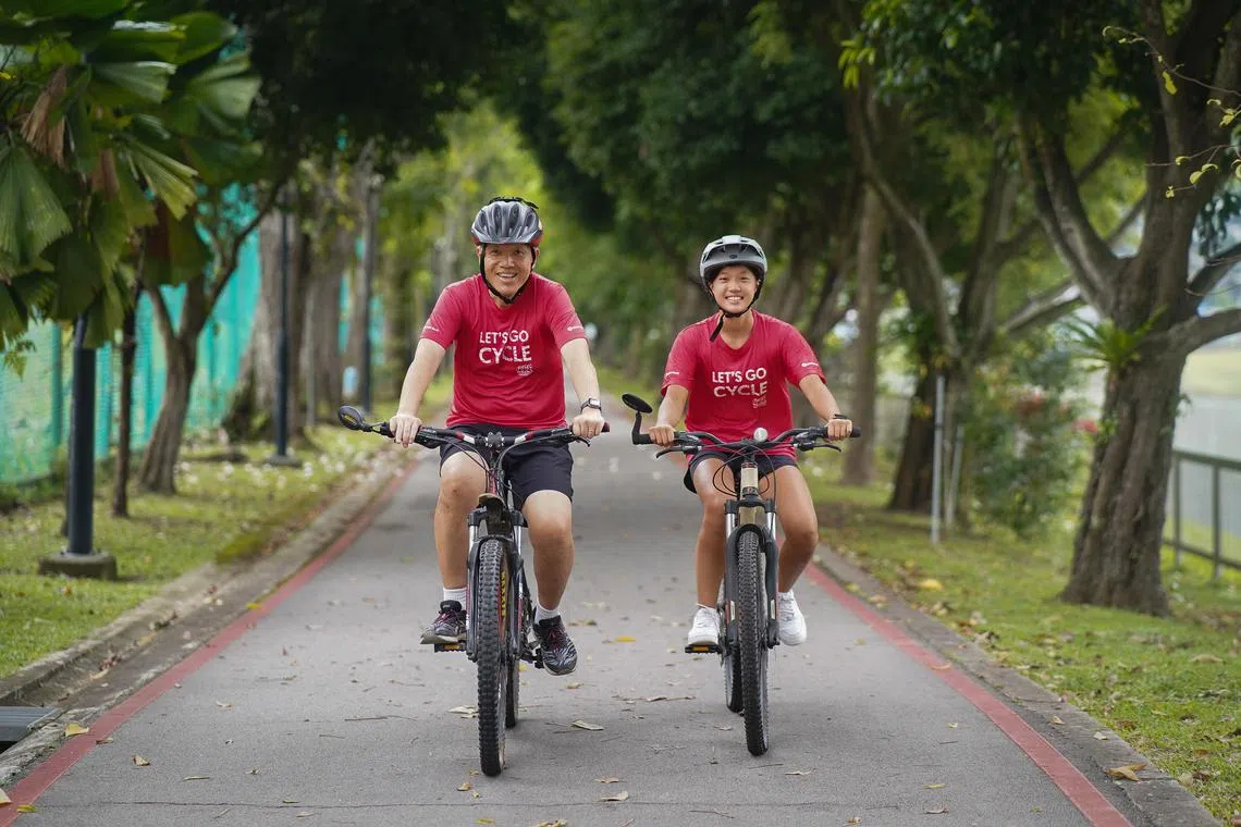 (left to right) David Sim, 52, civil servant, cycling with his daughter Dana Joy Sim, 15, student, at a park connector alongside ABC Waters @ Kallang River on 25 March, 2023. They have been participating in OCBC Cycle since Dana was 3 years old, and she will be cycling in her maiden The Straits Times 20km City Ride this year.