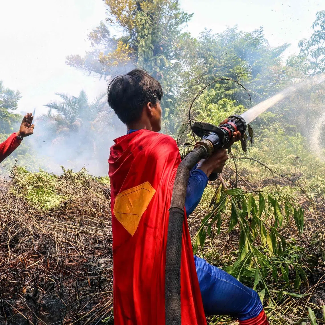 Indonesian student Rudiansyah (right) dressed in a Superman costume helps to extinguish a forest and land fire at Petuk Katimpun in Palangkaraya, Central Kalimantan, on Aug 17, 2026.
