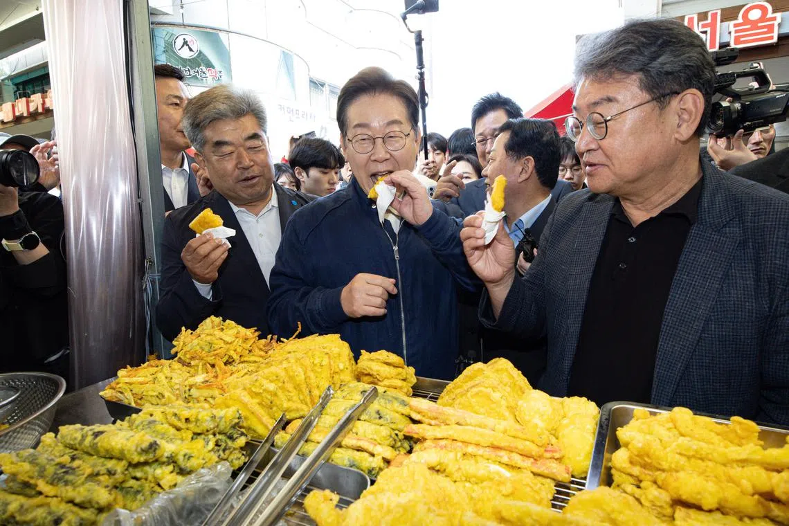 epa12068725 Lee Jae-myung (C), the Democratic Party candidate for the 03 June presidential election, tastes fried food during a visit to a traditional market in Cheorwon, Gangwon Province, South Korea, 02 May 2025.  EPA-EFE/YONHAP / POOL SOUTH KOREA OUT