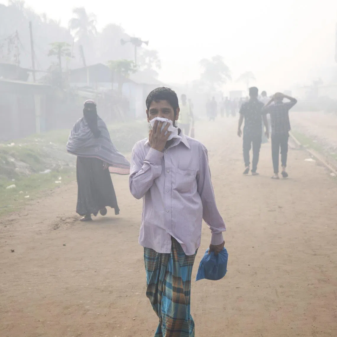 A man covers his mouth and nose as he walks along an area surrounded by smoke and dust in Shampur, Dhaka, on Feb 23, 2023. 