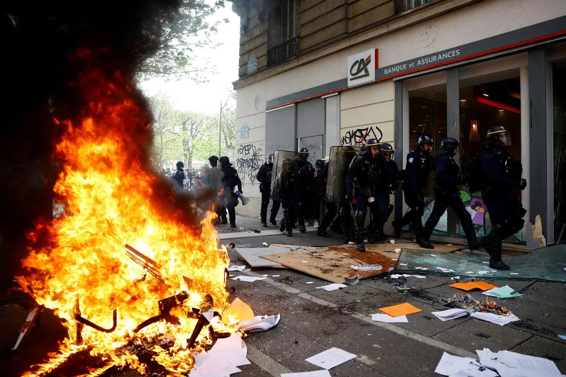 French CRS riot police take position in front of a destroyed Credit Agricole bank office near objects set on fire during the eleventh day of nationwide strikes.