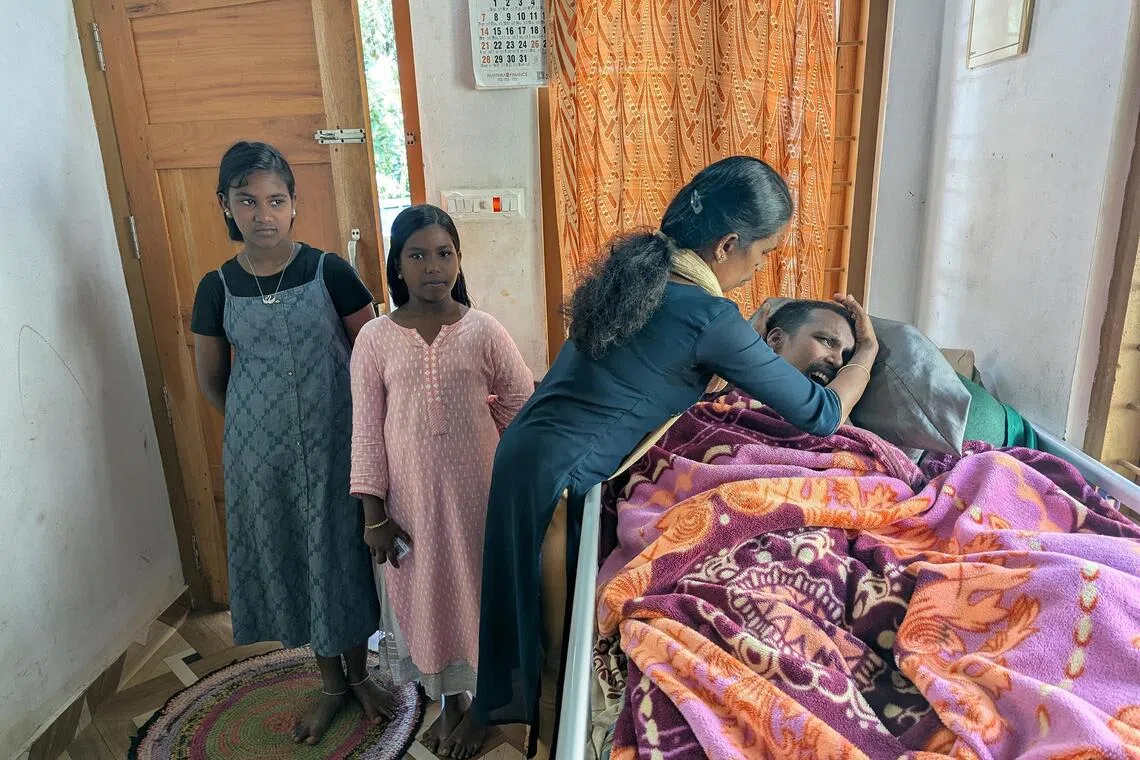 Mrs Parameshwari S. fixes her paralysed husband Selvam's pillow as her daughters look on. The family was listed as extremely poor in a Kerala state programme.