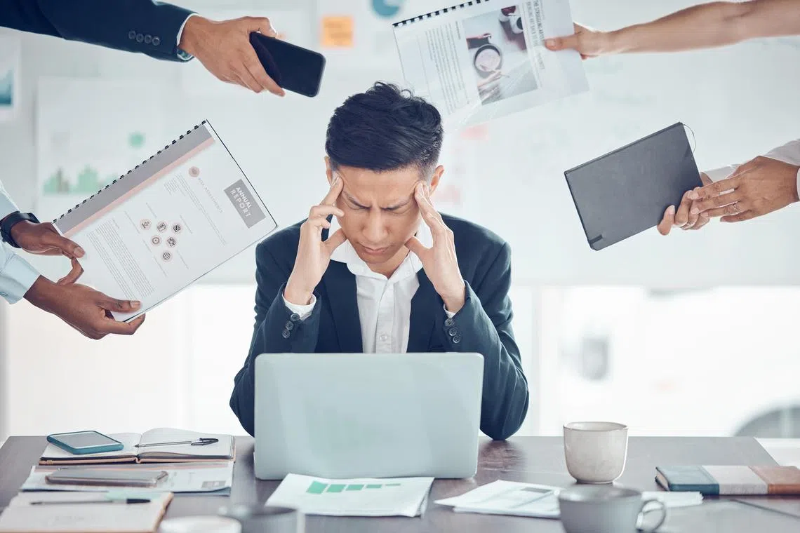 akbooks - Istockphoto - Stress, tired and business man with burnout, headache and frustrated work pressure with hands of employees giving task. Manager, mental health and data analyst male stressed and depressed at desk