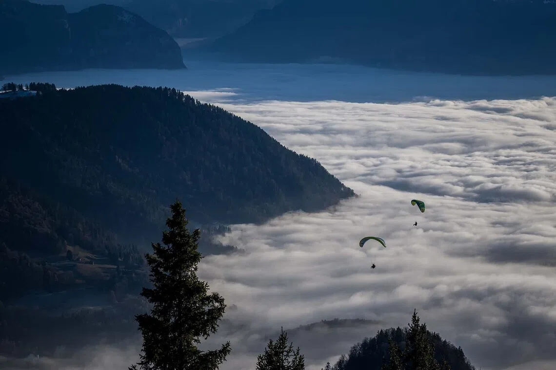 TOPSHOT - Paragliders soar above a sea of fog over the low-altitude resort of Leysin, western Switzerland on December 27, 2025. (Photo by Fabrice COFFRINI / AFP)