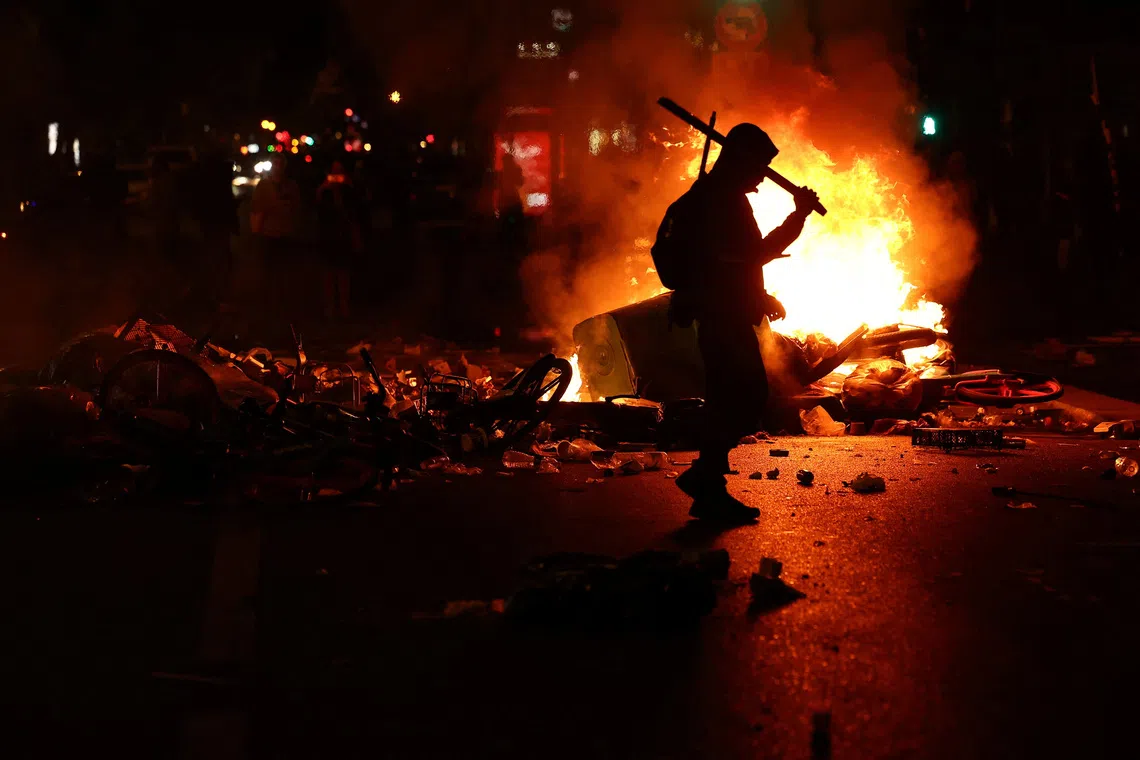 A person walks as flames rise during civil unrest, the day after a national day of demonstrations against the cost of living and rising fuel prices, in Paris, France, on Oct 18.