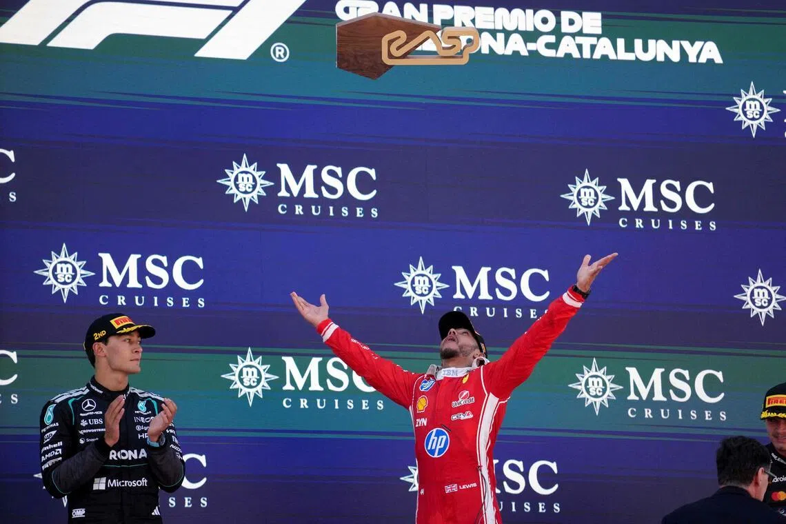 Ferrari's Lewis Hamilton celebrates by tossing his trophy into the air after winning the Barcelona-Catalunya Grand Prix as his former teammate George Russell (left) of Mercedes and McLaren's Lando Norris (right) watch on.