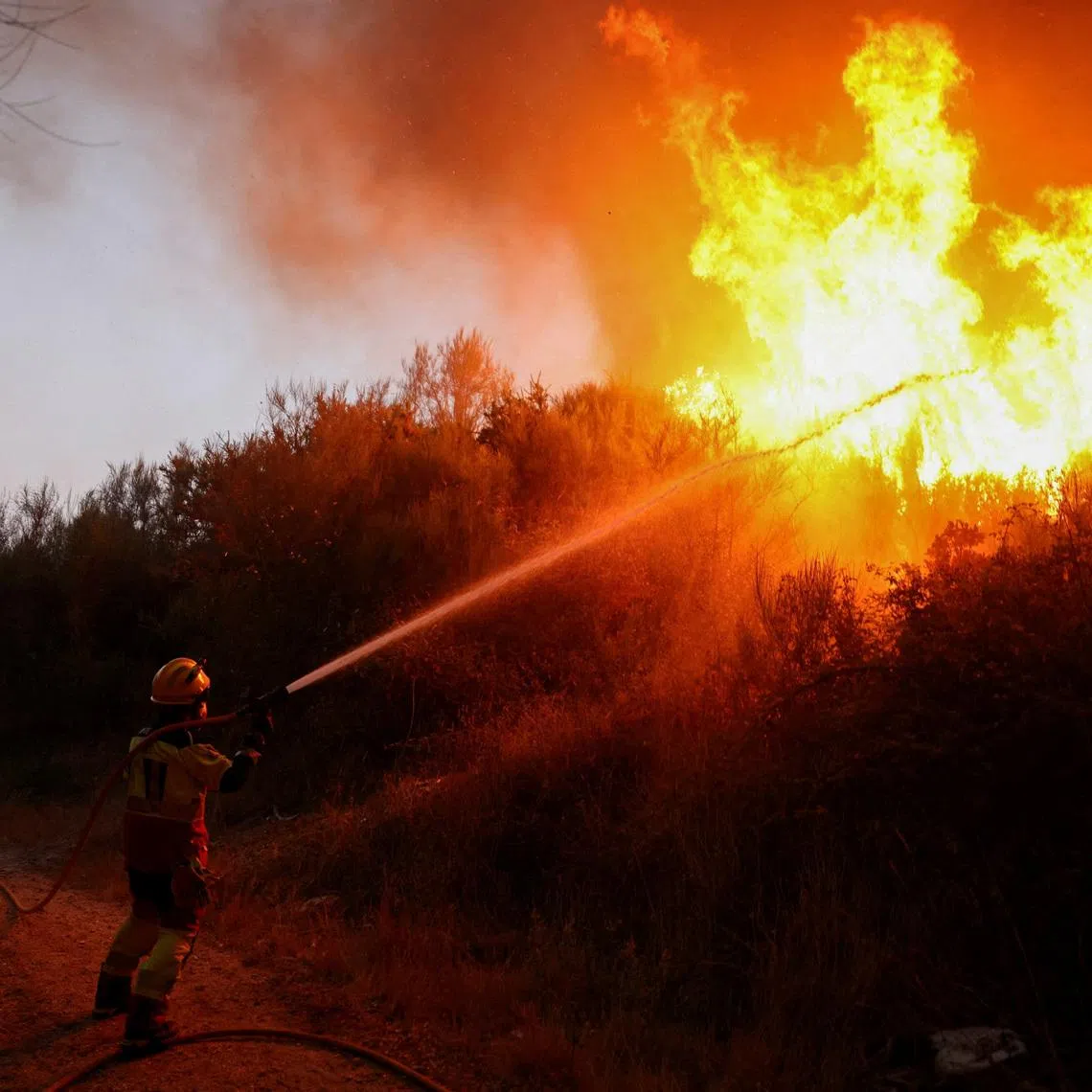 FILE PHOTO: A firefighter uses a hose as smoke and flames from a wildfire rise in Vilar de Condes, in the province of Ourense in Galicia, Spain, August 15, 2025. REUTERS/Nacho Doce/File Photo