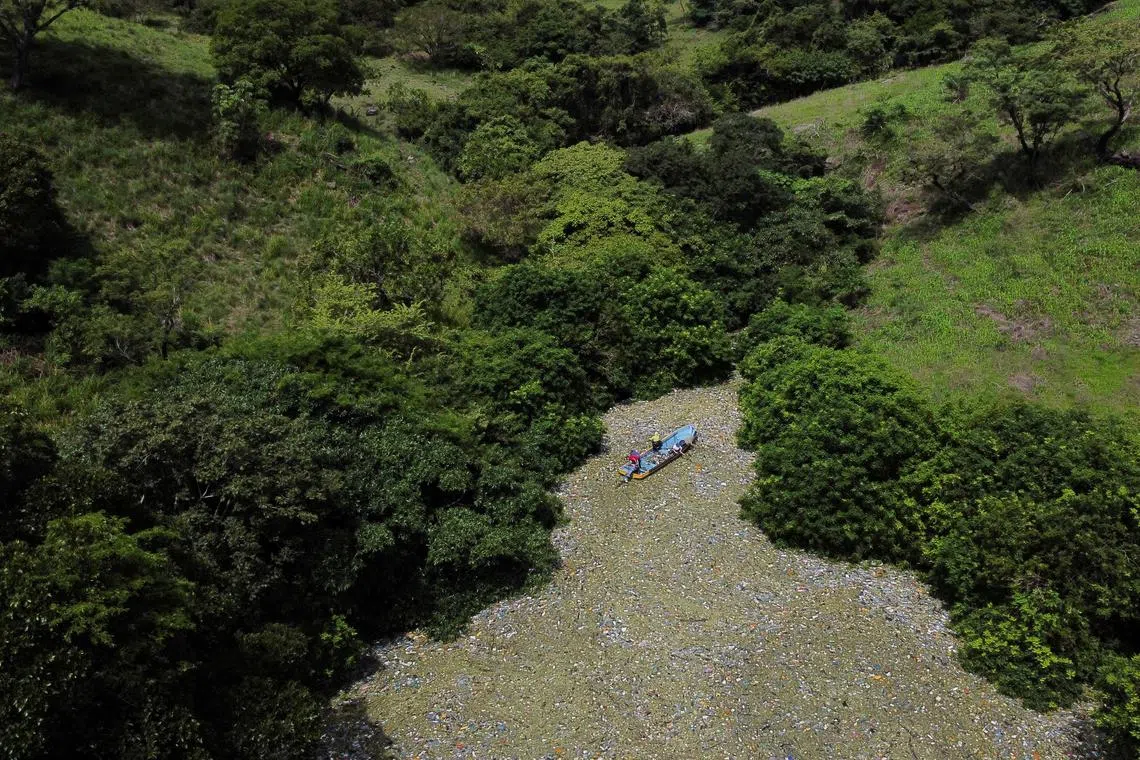 People navigate among trash as they work in a program funded by Salvadoran government to clean the the El Cerron Grande reservoir in Potonico, El Salvador September 14, 2022. REUTERS/Jose Cabezas/File Photo