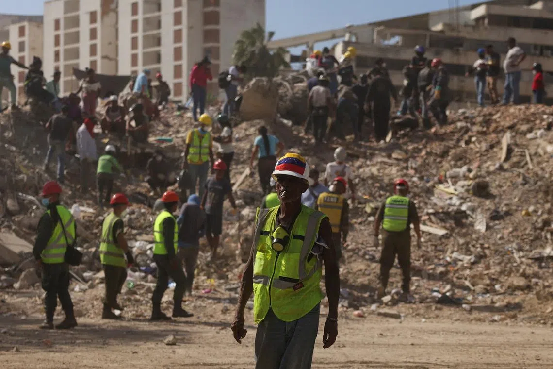 A search and rescue volunteer wearing a Venezuelan flag attached to his helmet searches debris alongside other people, in the aftermath of the June 24 earthquakes, in La Guaira, Venezuela, July 16.
