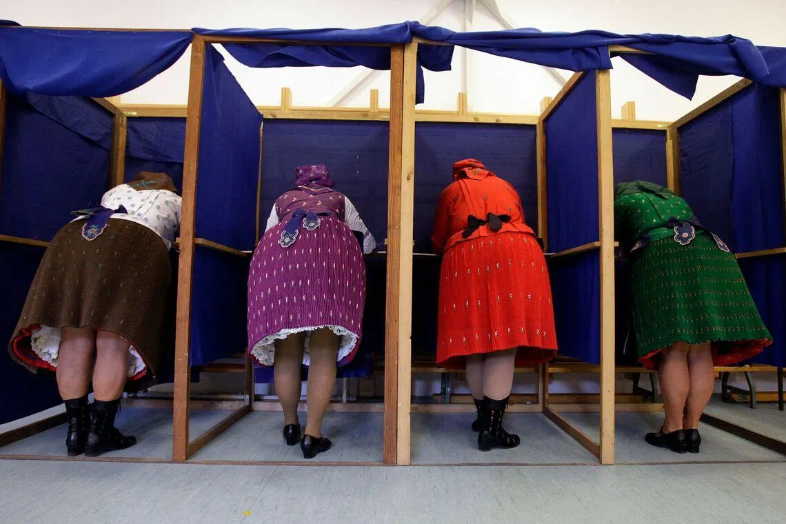 TOPSHOT - Women in traditional Hungarian dresses fill out their ballot papers at a polling station in a nursery school in Veresegyhaz, some 30km east of Budapest, on April 12, 2026, during the general election in Hungary. The vote could end Hungarian Prime Minister Viktor Orban's 16-year stint in power as the EU's longest serving current leader and a self-decribed "thorn" in the bloc's side. (Photo by Peter Kohalmi / AFP)