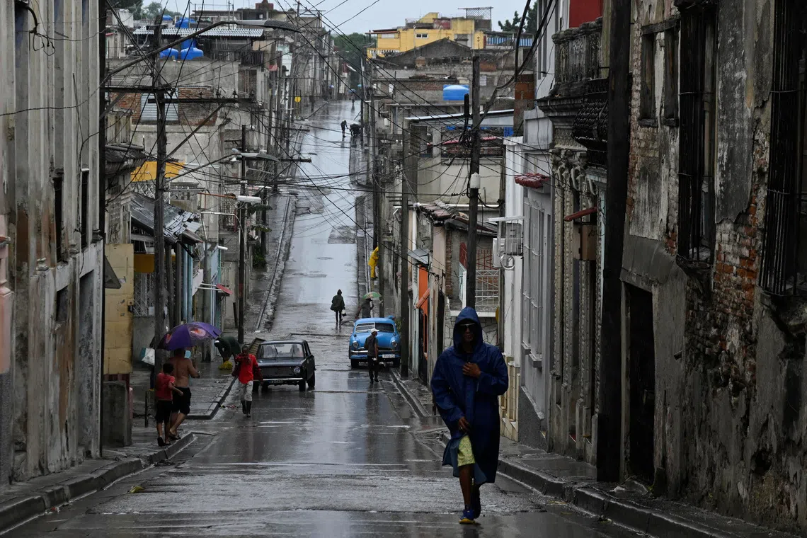 People walk along a street in the rain ahead of Hurricane Melissa's landfall, in Santiago de Cuba, Cuba, October 28, 2025. REUTERS/Norlys Perez