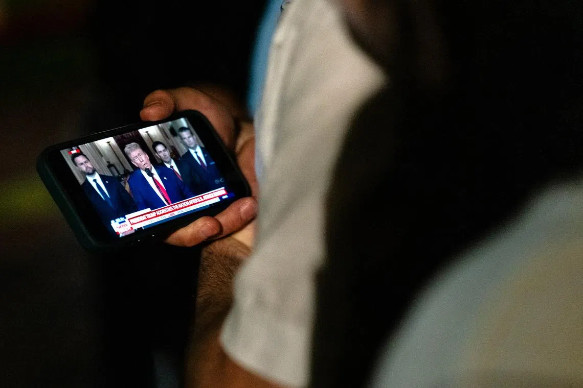 People watch US President Donald Trump deliver his remarks on their phones as they stand outside the White House on June 21.