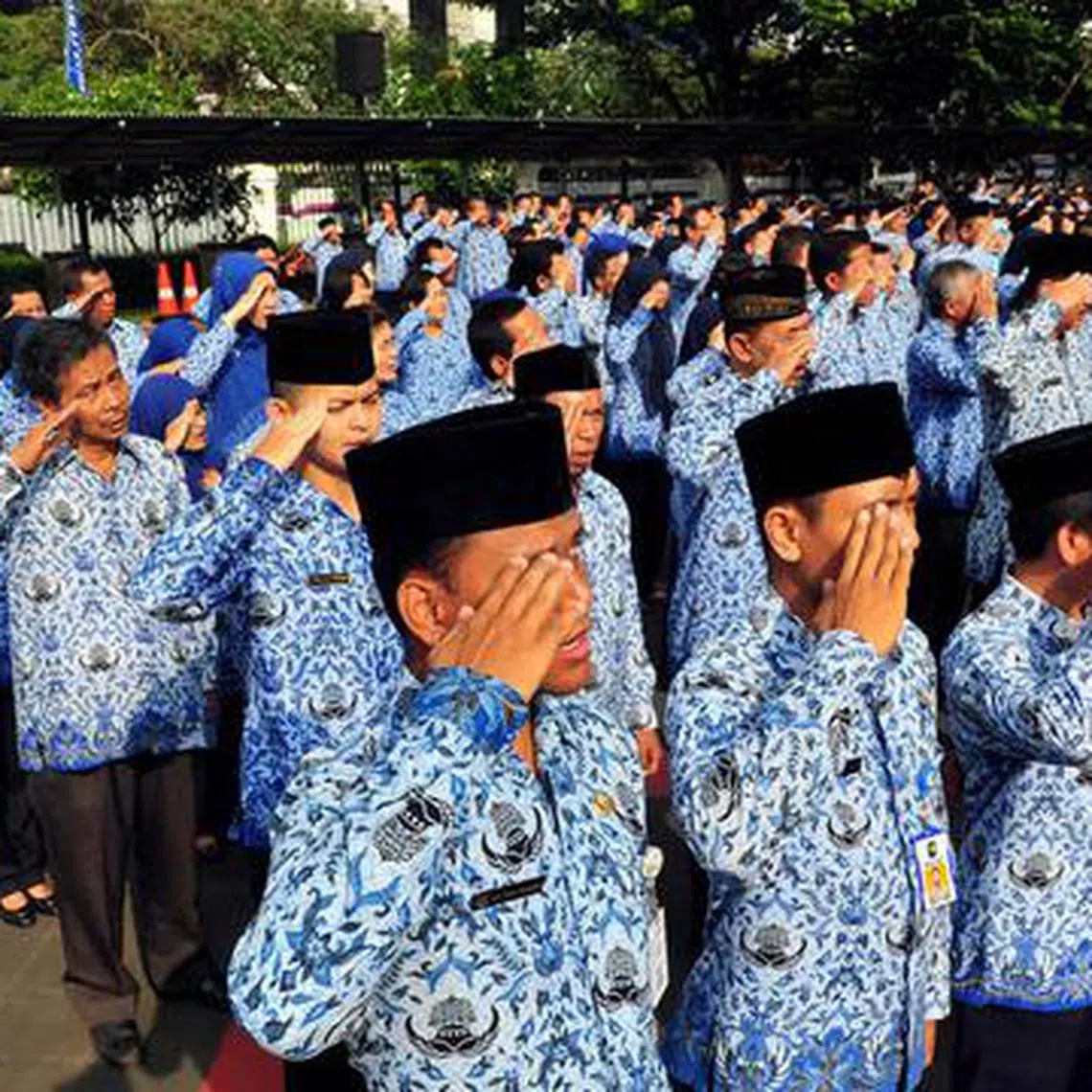 Civil servants in Jakarta saluting the flag while singing the national anthem during a ceremony (no date).  Government workers are facing work disruptions following big budget cuts.
