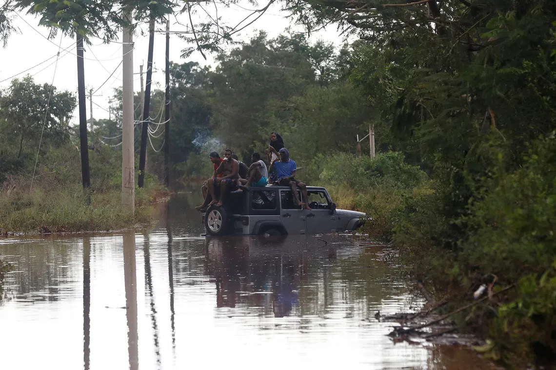 People sit on the roof of a vehicle riding on a flooded road, after Hurricane Melissa made landfall, in Prospect, Manchester, Jamaica, October 29, 2025. REUTERS/Octavio Jones