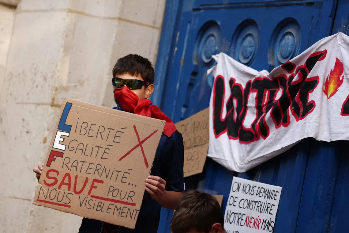 A masked high school student holds a placard reading \"Liberty, Equality, Fraternity. Except for us, apparently\" during a gathering outside the Lycee Voltaire high school in Paris as part of a nationwide day of demonstrations and blockades, voicing anger over overcrowded classrooms, teacher shortages and dilapidated school buildings, which students blame on years of underinvestment, France, October 6, 2026. REUTERS/Tom Nicholson