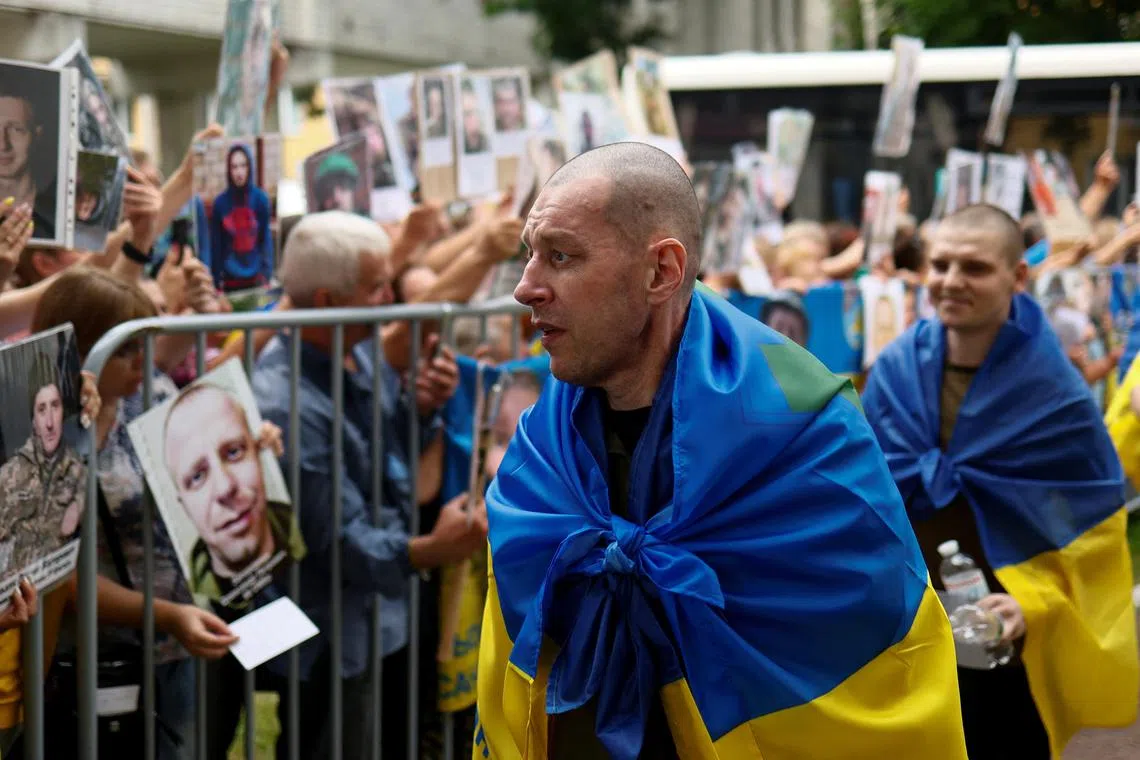 Relatives holding up photos of their missing family members on July 4 as freed Ukrainian prisoners of war return home, in the hope that they might recognise the people in the photos.