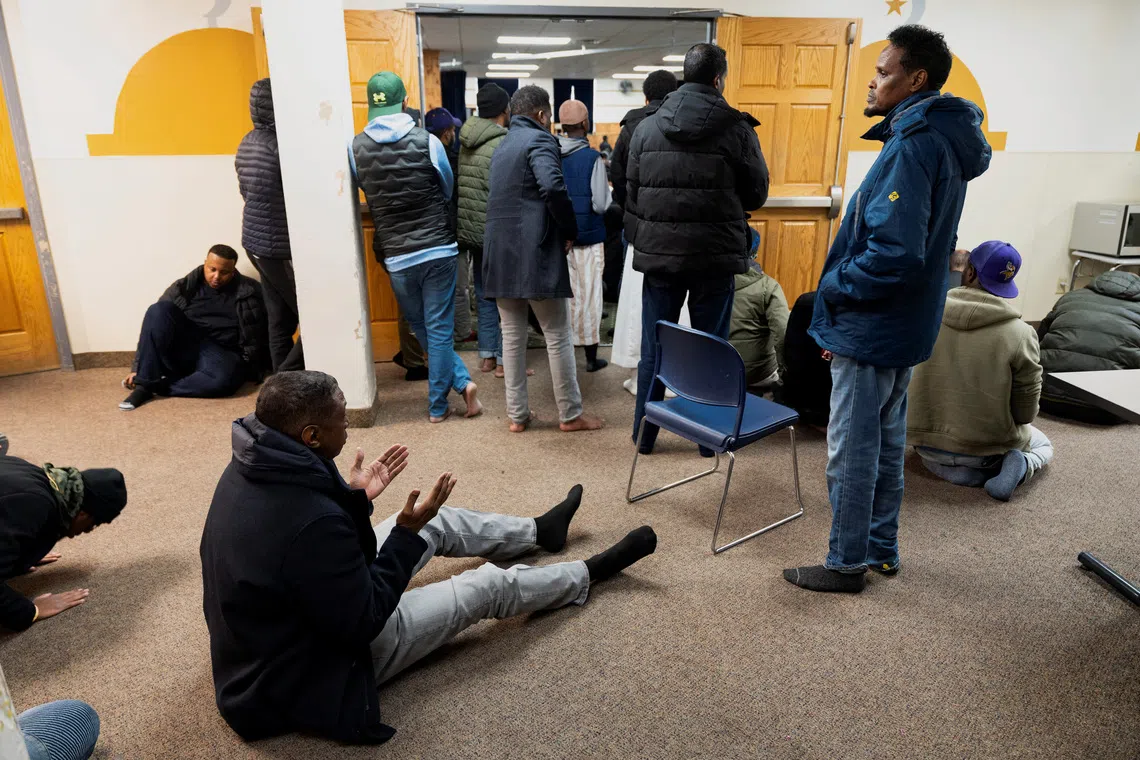 Men gathered in a room, some standing and others sitting or kneeling on the floor.