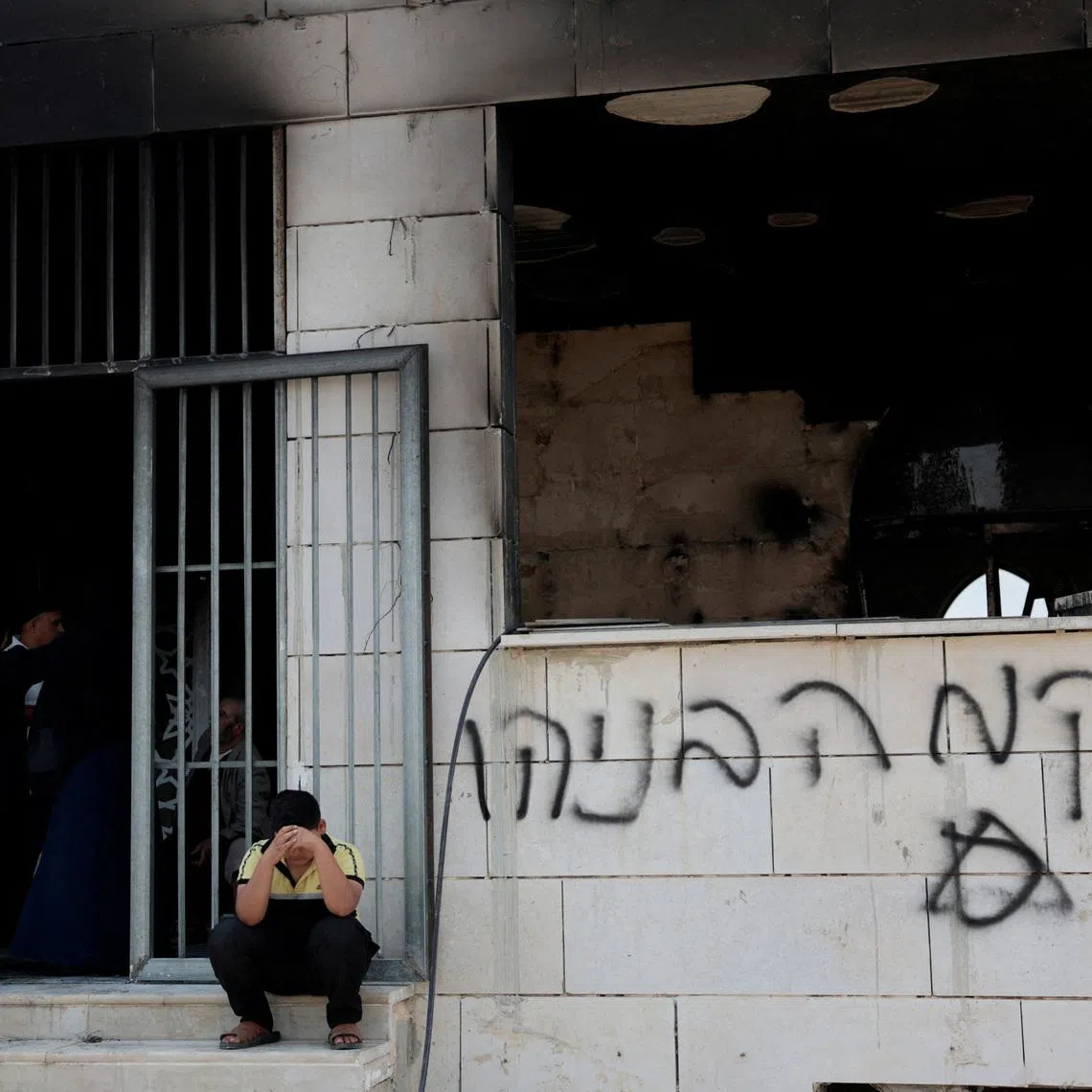A boy sits near a damaged mosque, which Palestinians say was damaged by Israeli settlers, in West Bank on July 26.