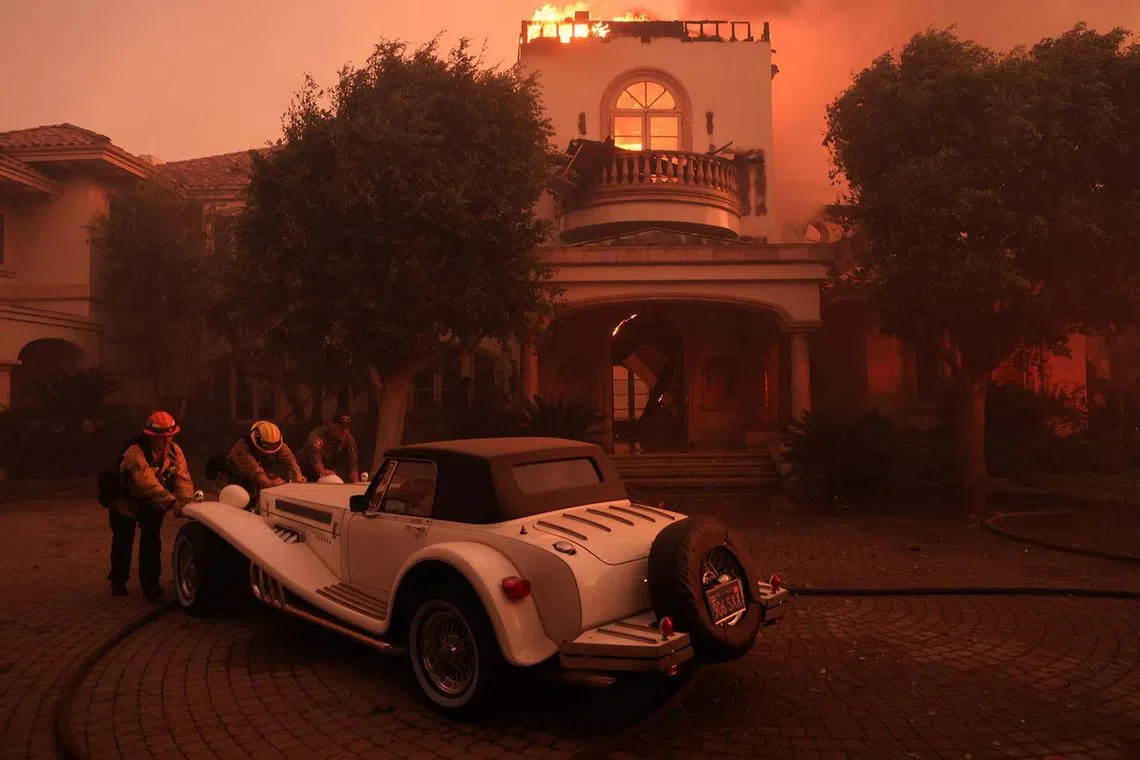 Rescue workers pushing a vintage car as smoke billows from the Mountain Fire in Camarillo, California, US, Nov 6, 2024. 
