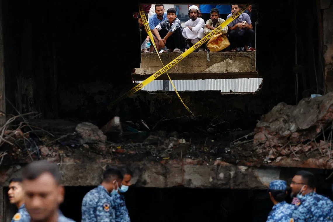 On lookers watch through a damaged window as members of Bangladesh Air Force work at the site, after an air force training aircraft crashed into a building belonging to Milestone School and College, in Dhaka, Bangladesh, July 22, 2025. REUTERS/Mohammad Ponir Hossain