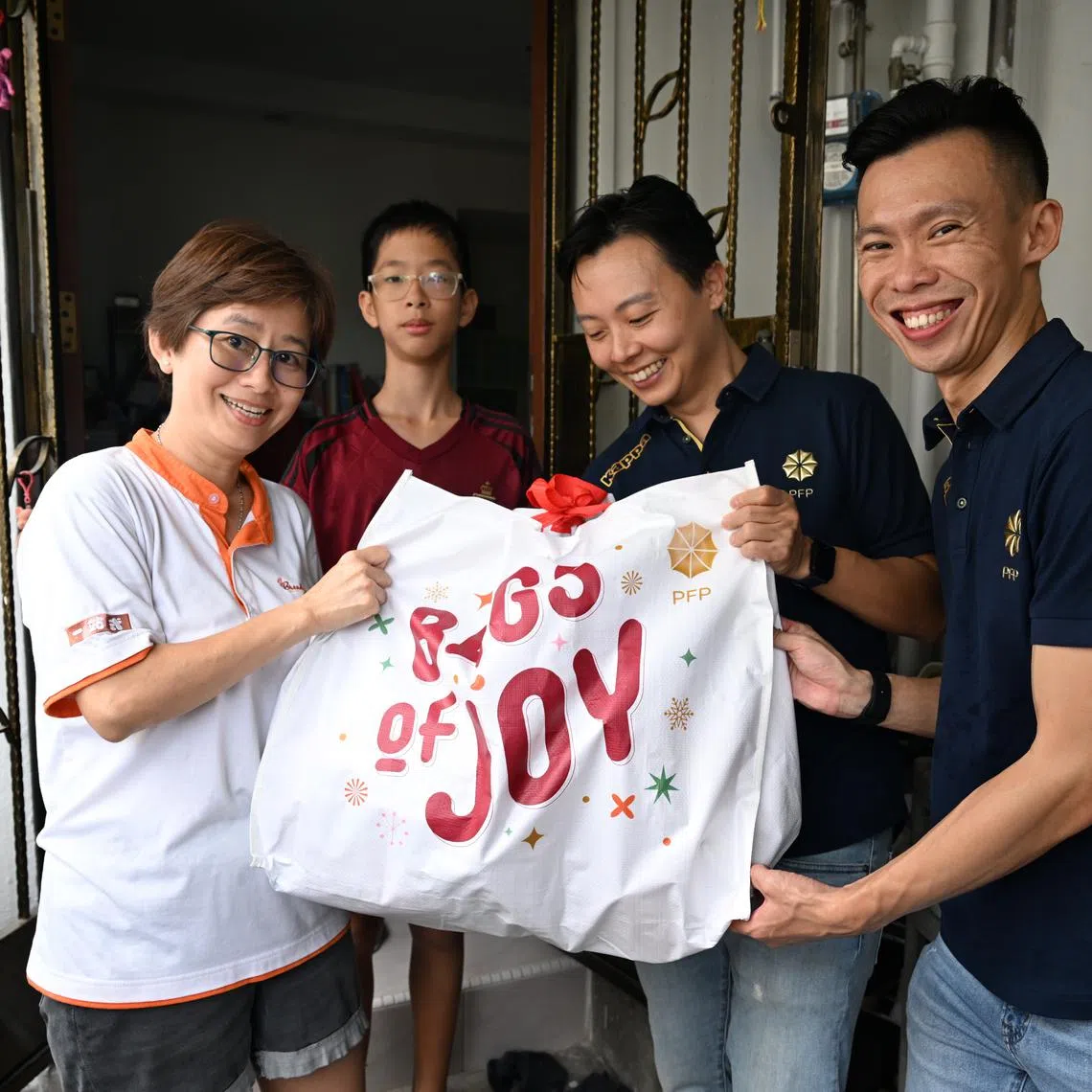 (From left) Beneficiaries Jane Lim and her son Yew Zhe Hao receiving a "bags of joy” goodie bag from financial advisors Chew Shu Xiang and Samuel Koh.